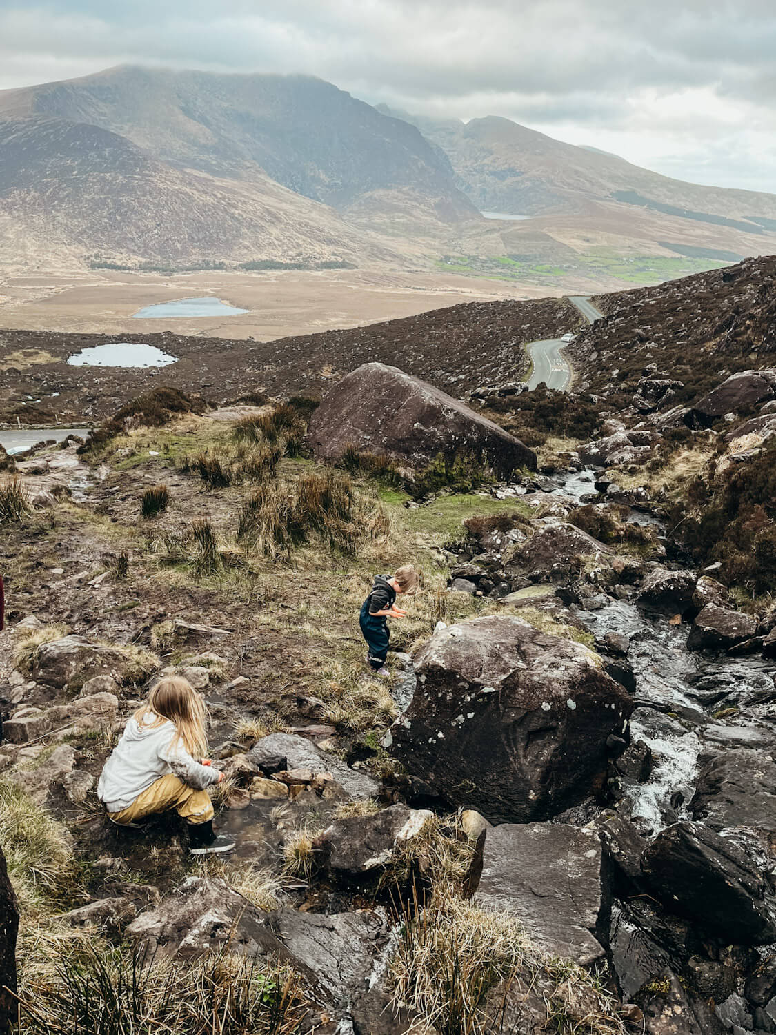 Two children play near stream with views of lakes and mountains on Conor Pass Ireland