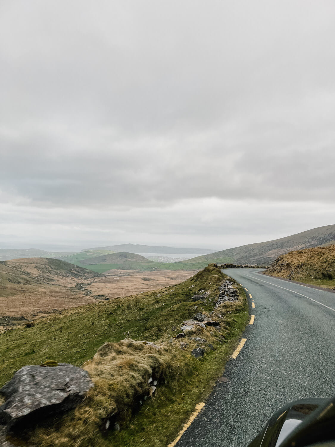 View of green hills and the sea from a narrow winding road