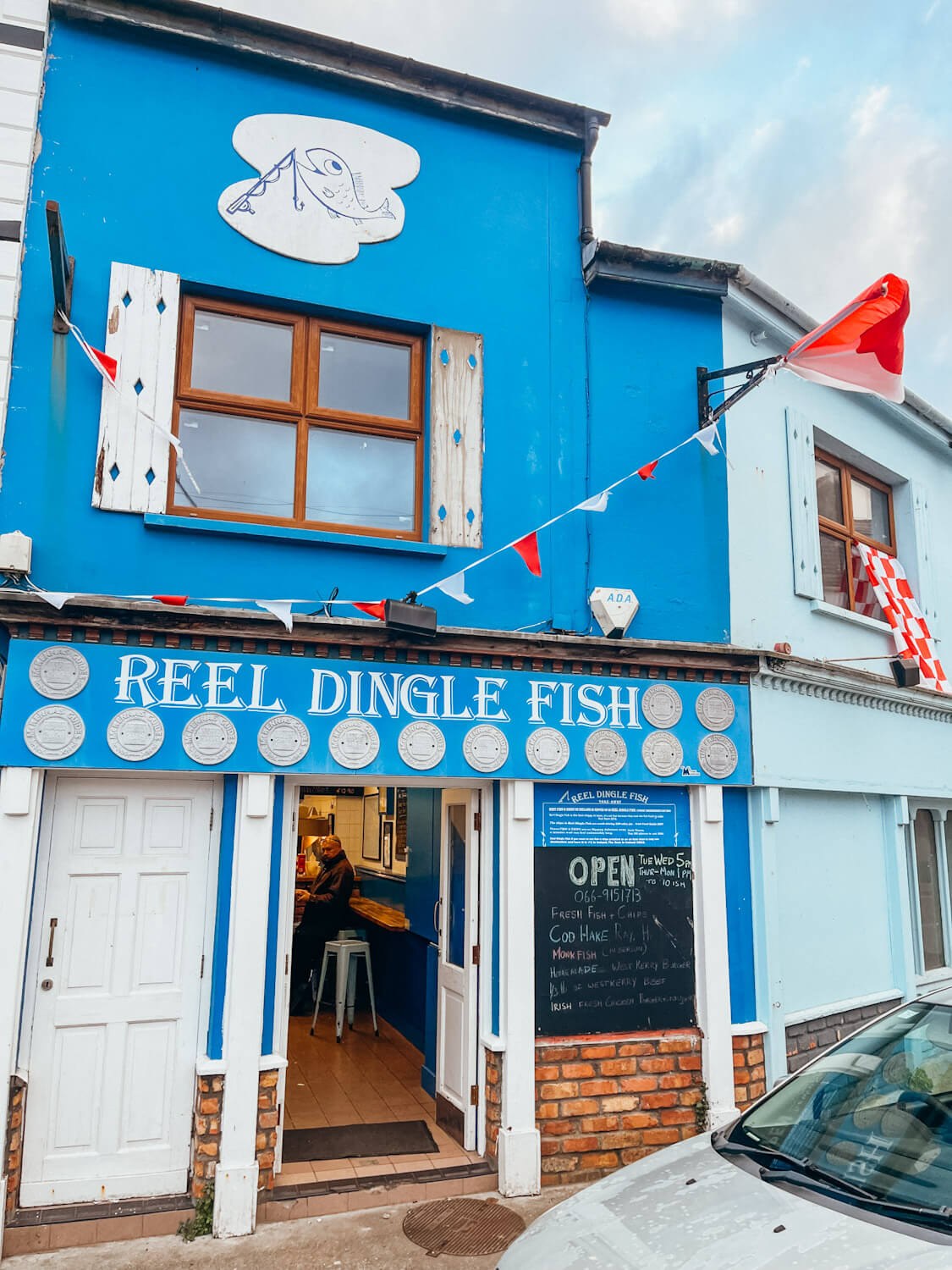 Blue and white store front with red and white flags flying in Dingle Ireland