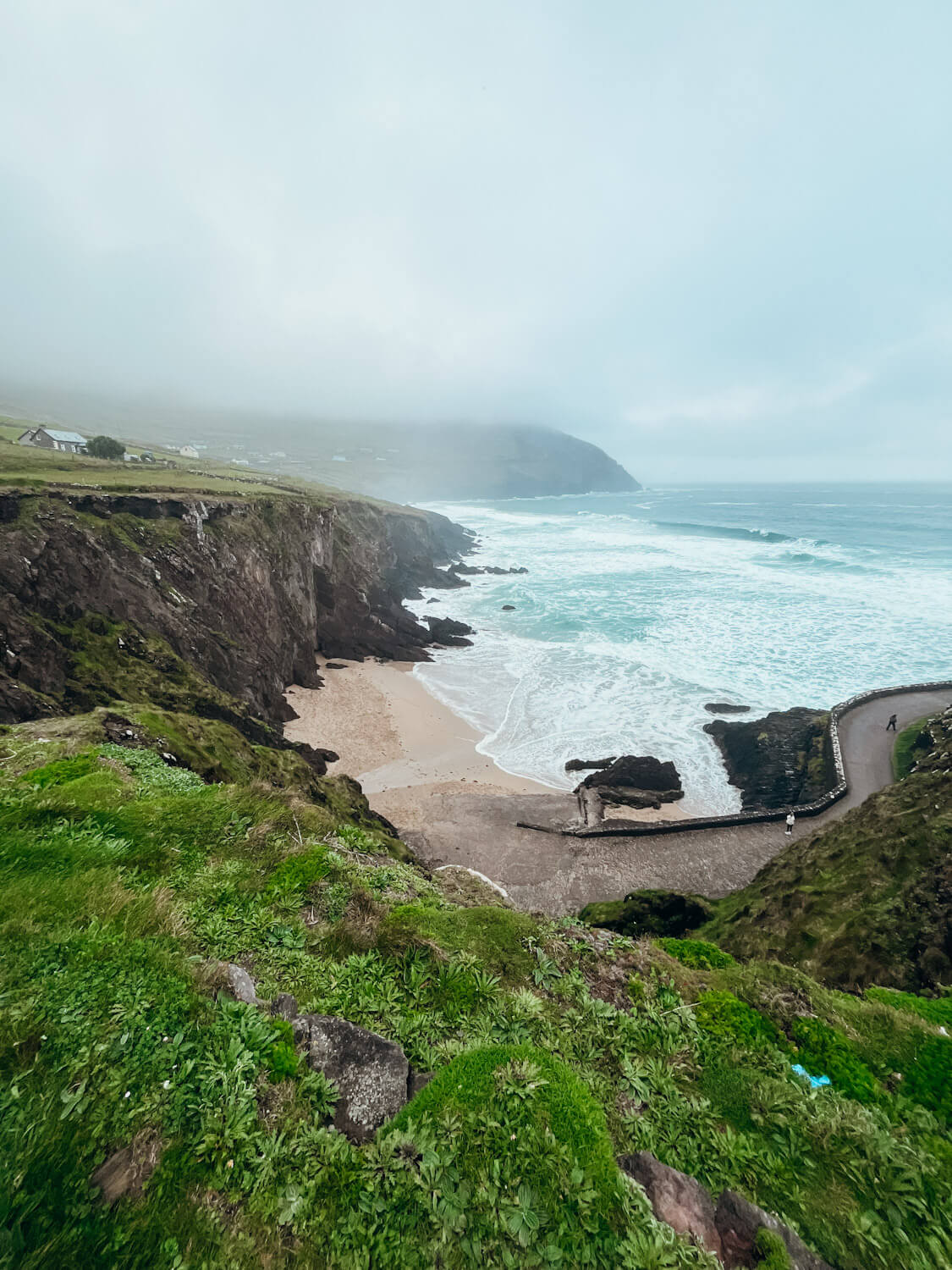 View of sandy beach lined with green grassy cliffs in Dingle Ireland