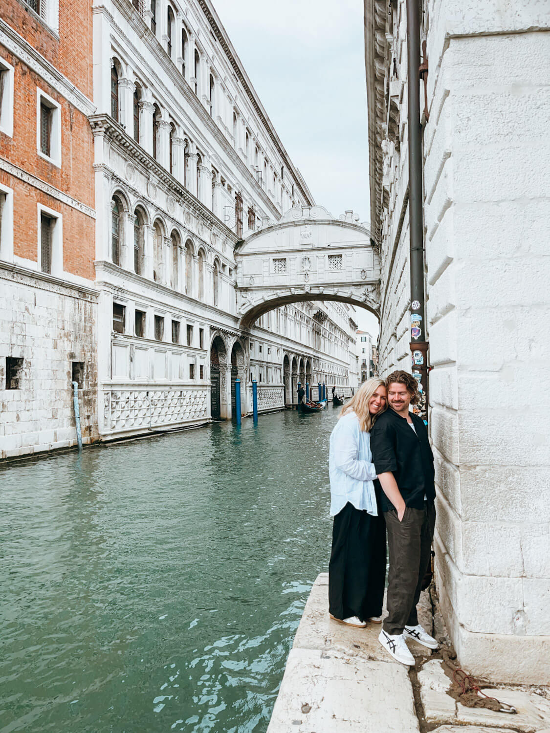 Couple stand in front of white stone bridge in Venice (Bridge of Sighs)