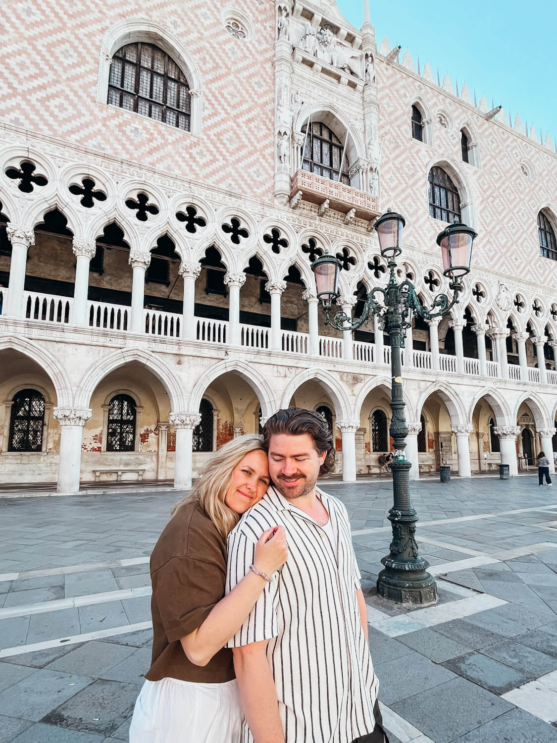 Couple stands in front of the ornate, white arches of Doge's Palace in Venice