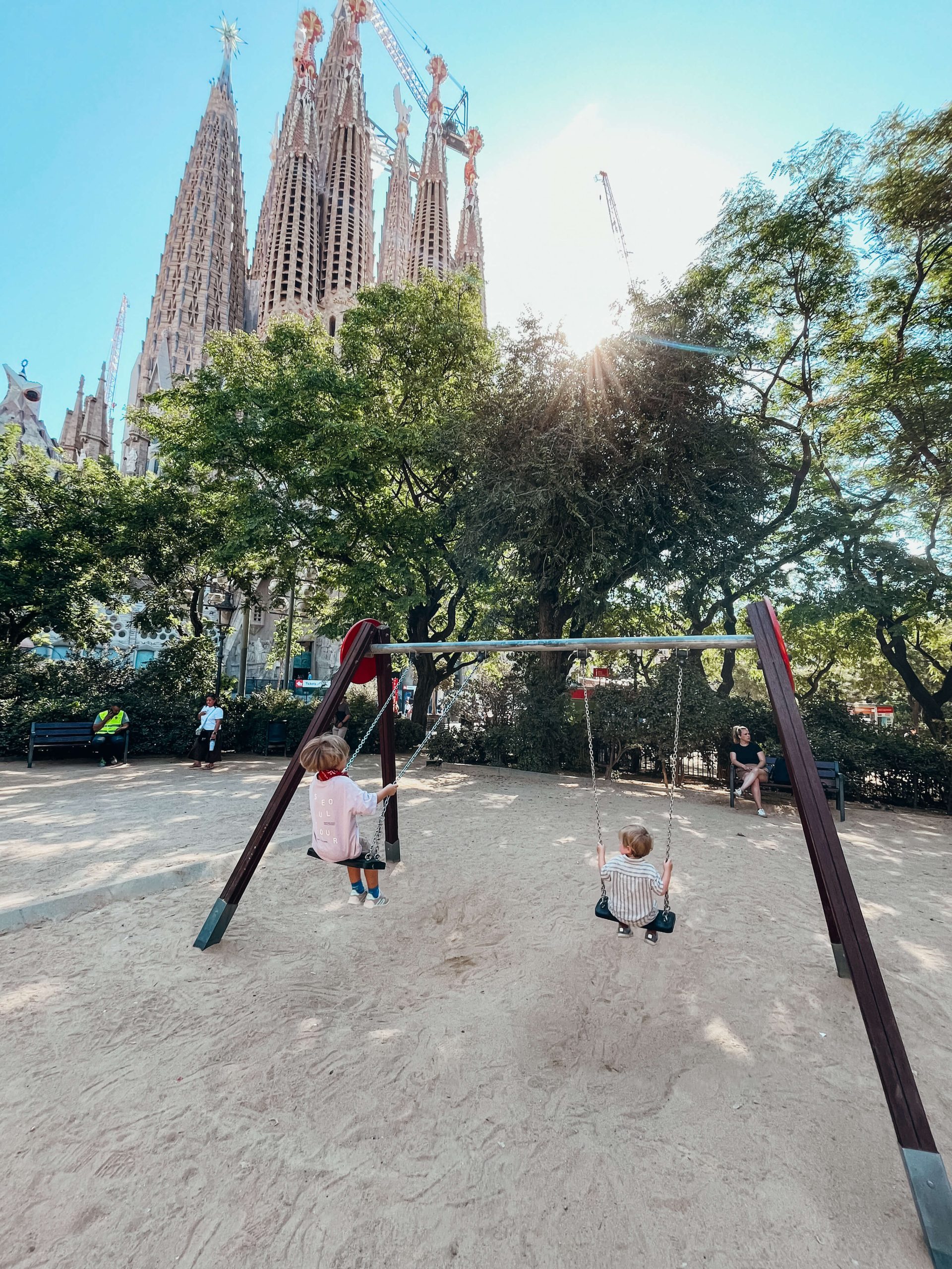 Kids swing on swingset with Sagrada Familia in the background
