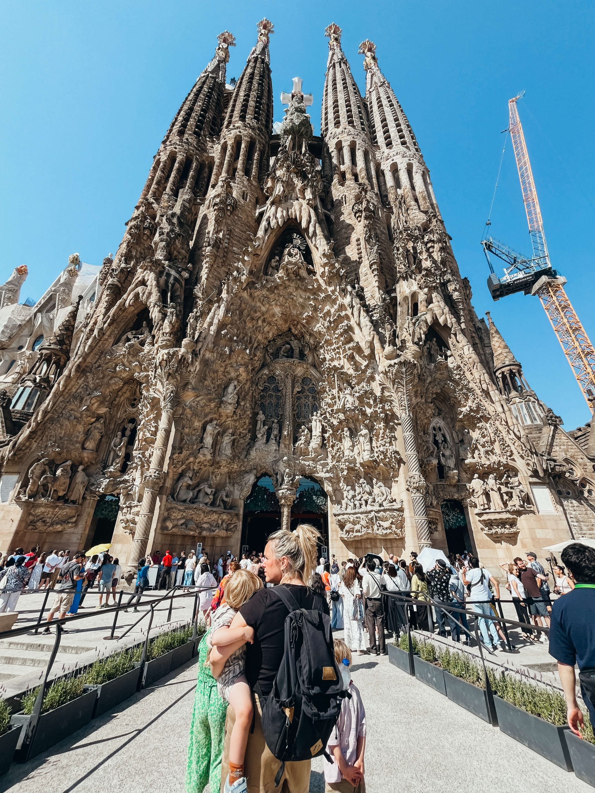 Woman and children stands facing Sagrada Familia in Barcelona with kids