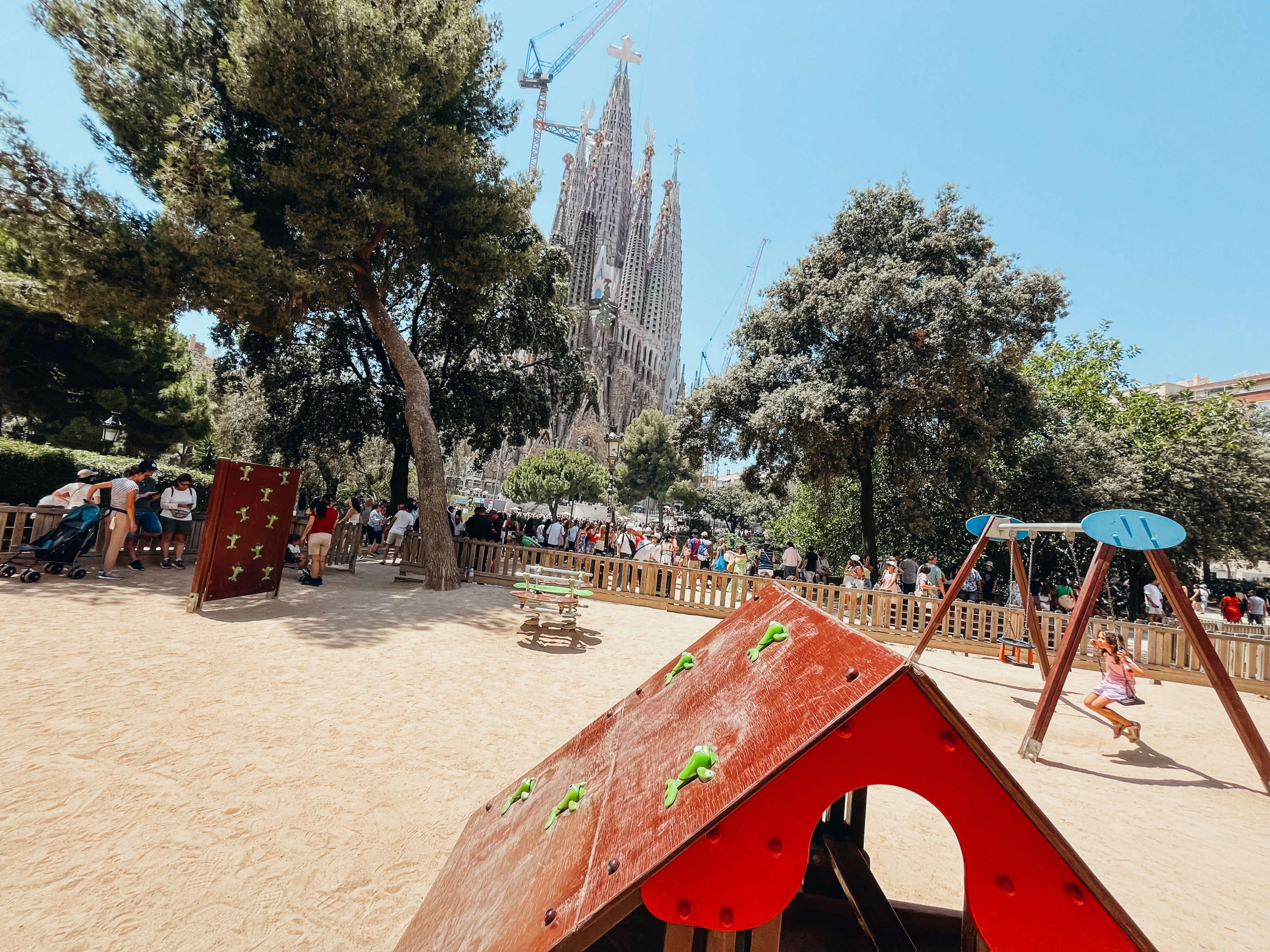 Playground with small play structures and sand with Sagrada Familia in the background