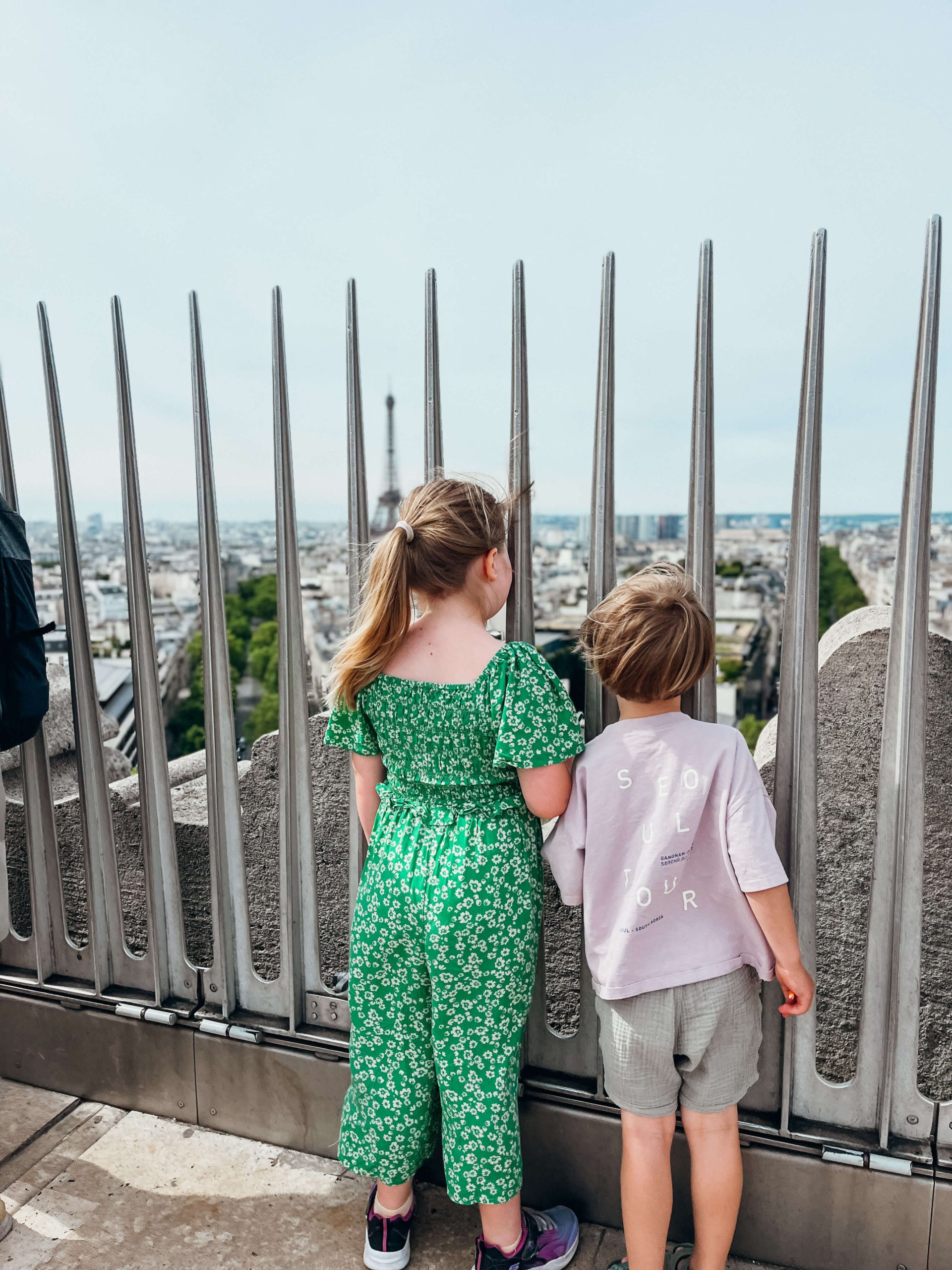 Two children look at view of Eiffel Tower from the top of the Arc de Triomphe with kids