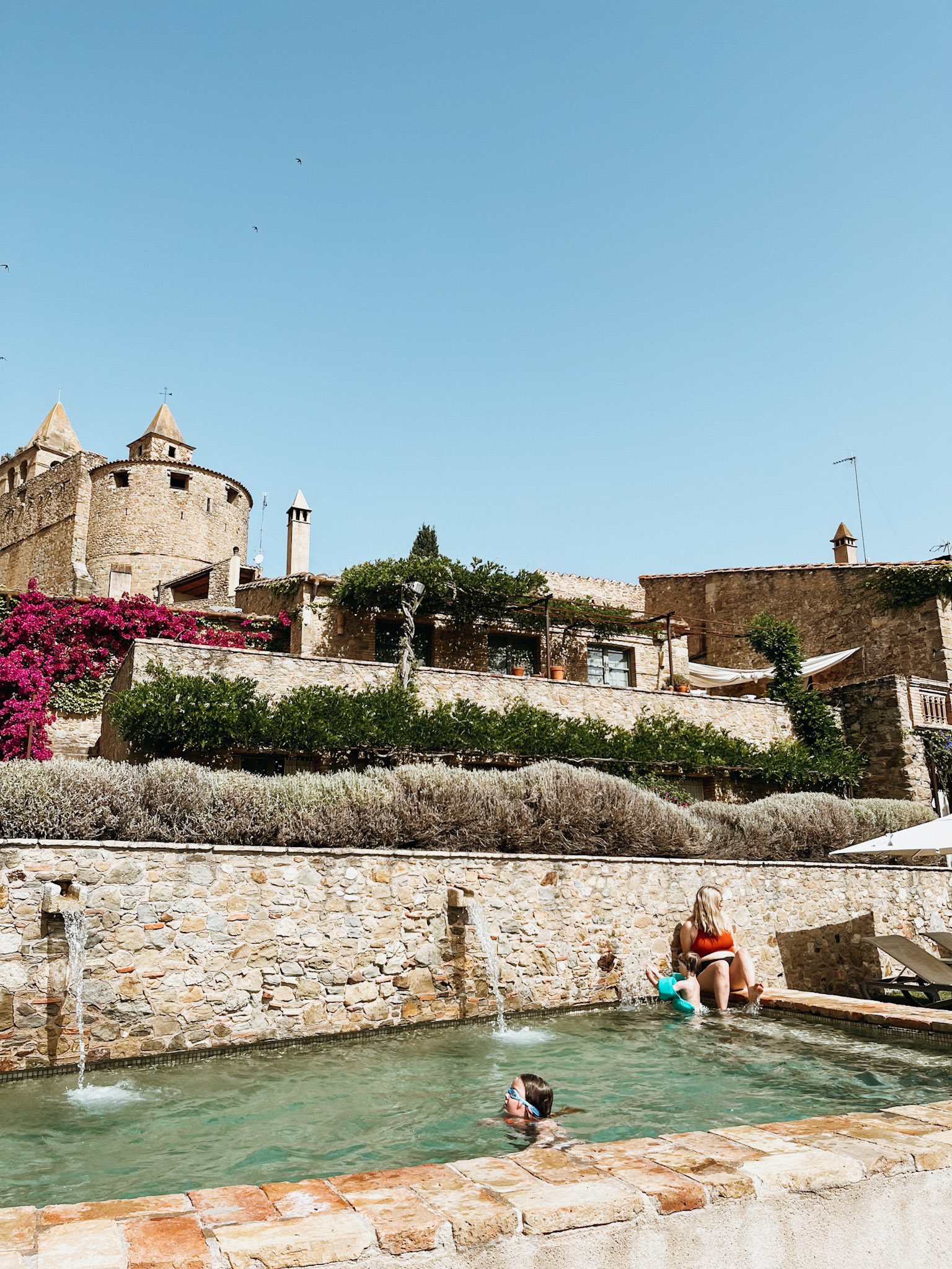 Restored brick farmhouse complex in spain with vines and pink flowers with a pool in the foreground- best place to stay in can bassa in june