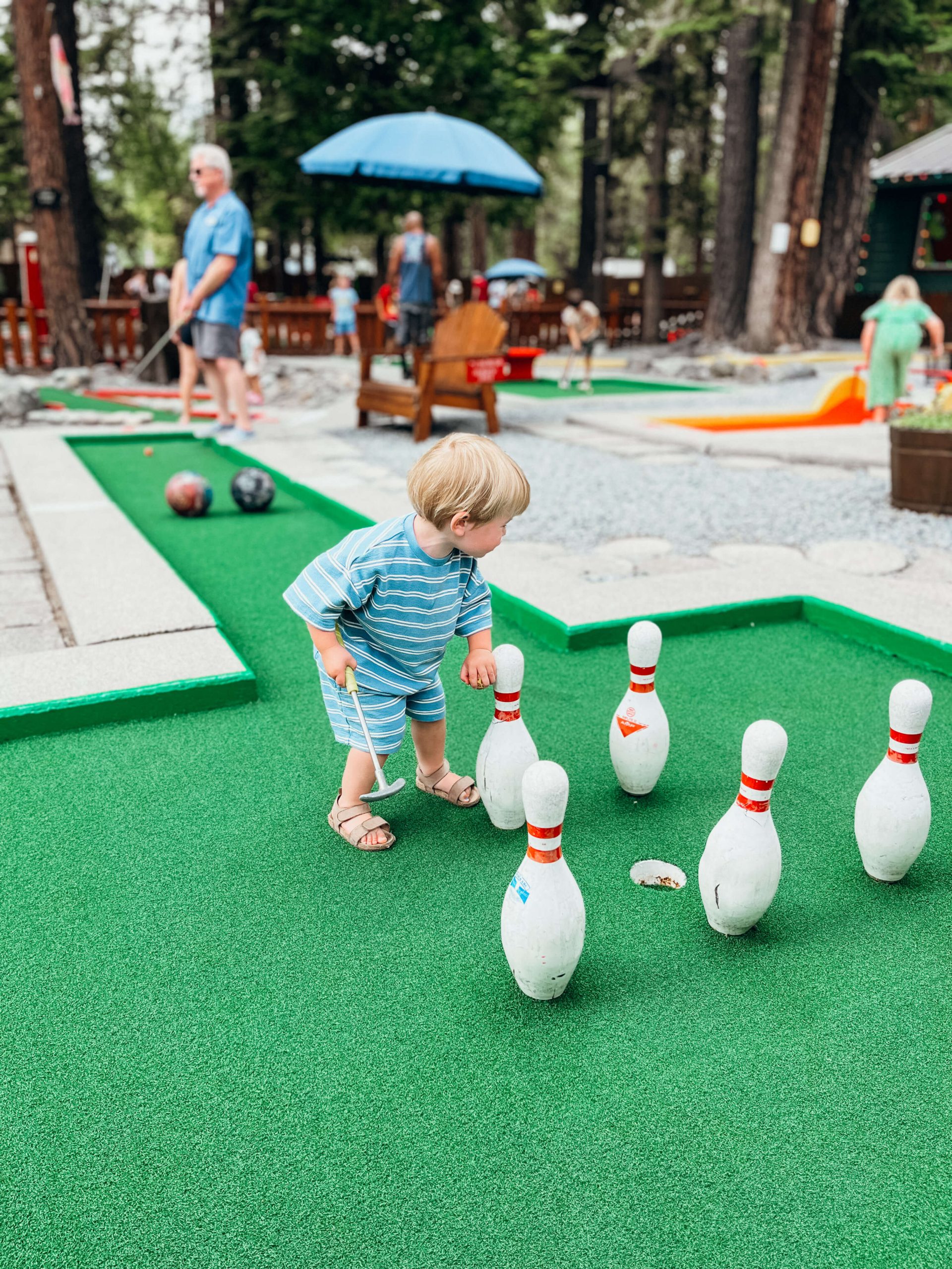 Little boy stands near stationary bowling pins near a hole at King's Beach Mini Golf