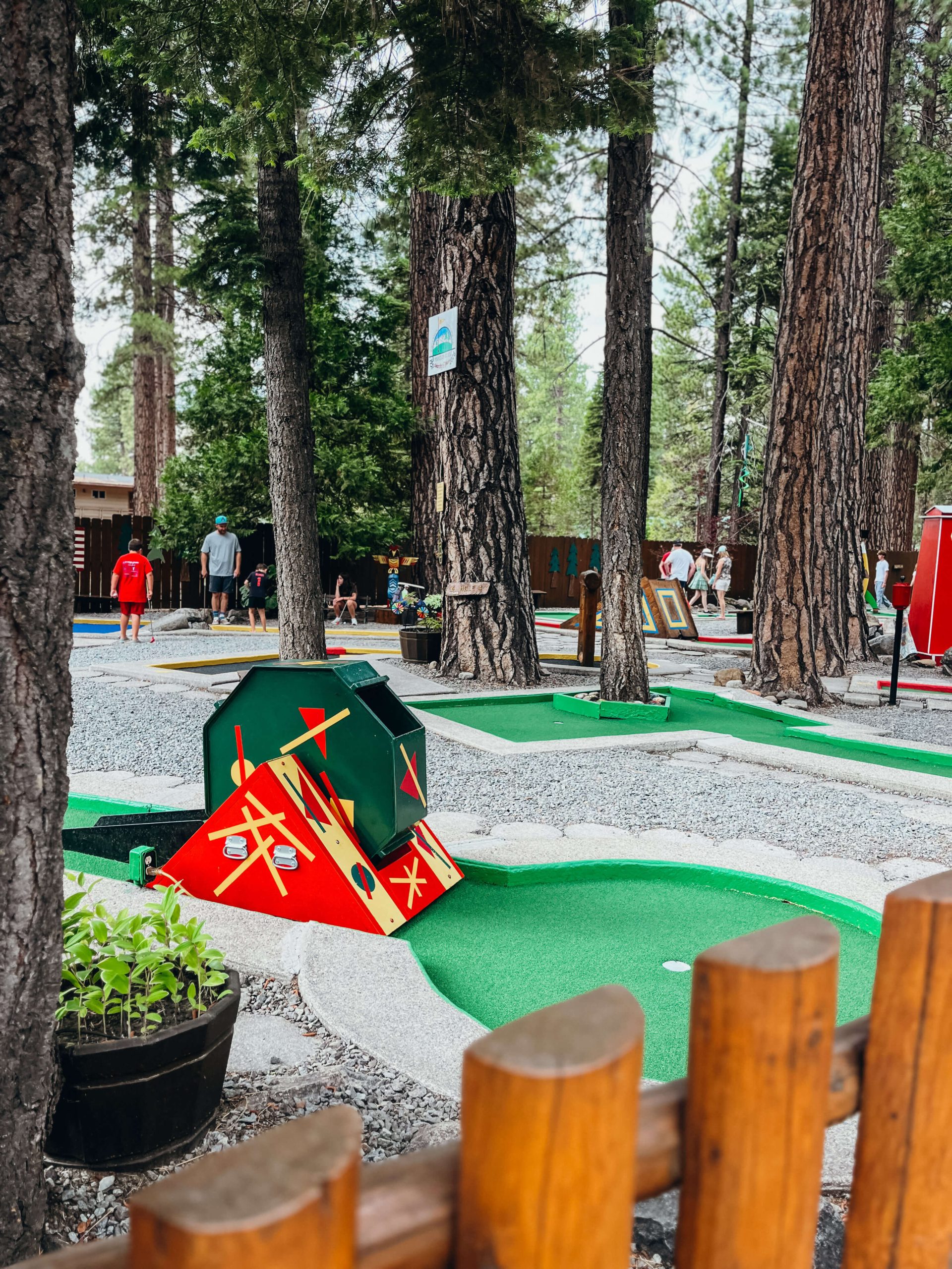 Large, green and yellow moving trap on a hole with tall pine trees in the background at King's Beach mini golf