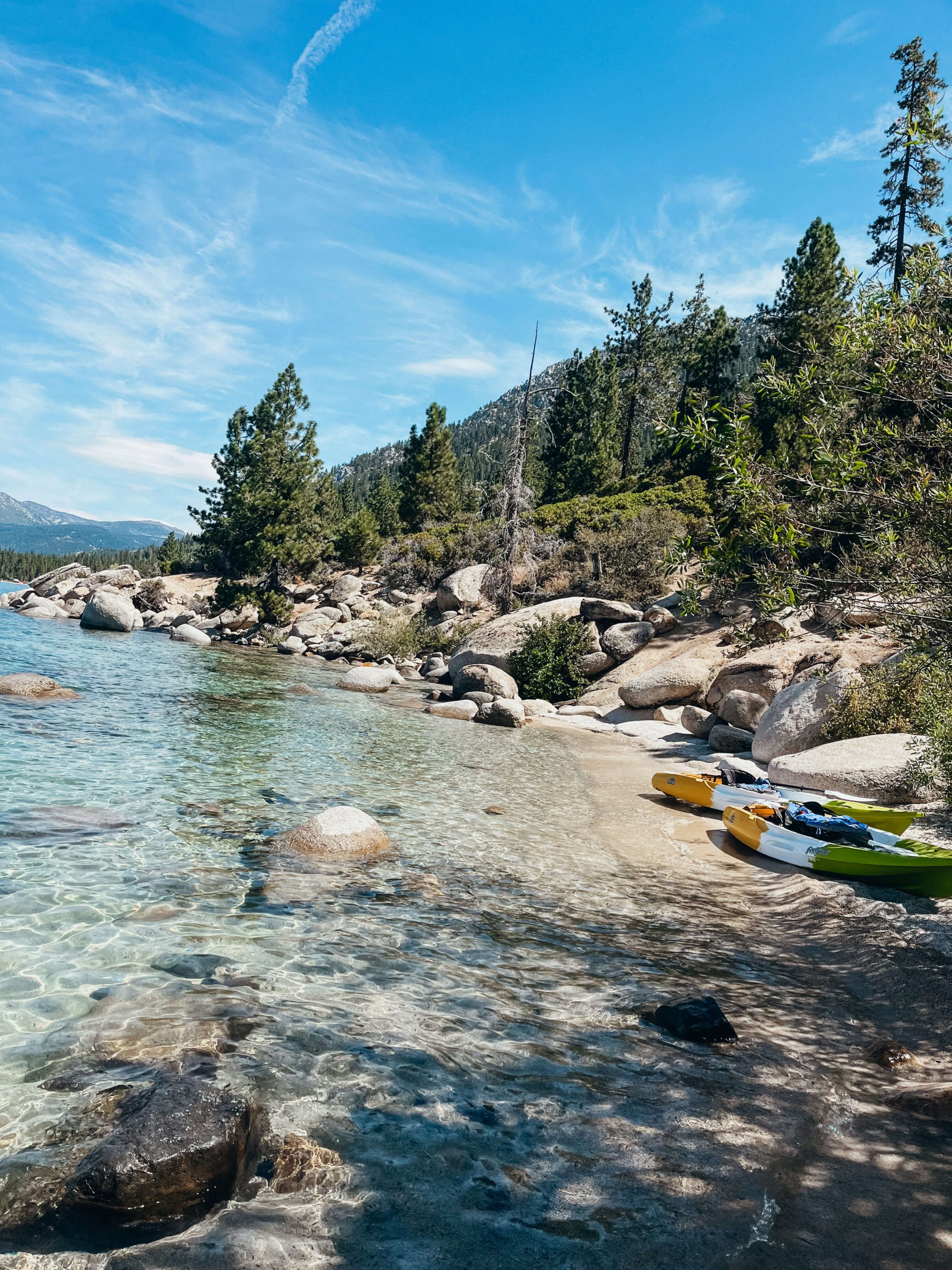 Two kayaks pulled up on small, sandy beach with boulders and pine trees at Lake Tahoe 