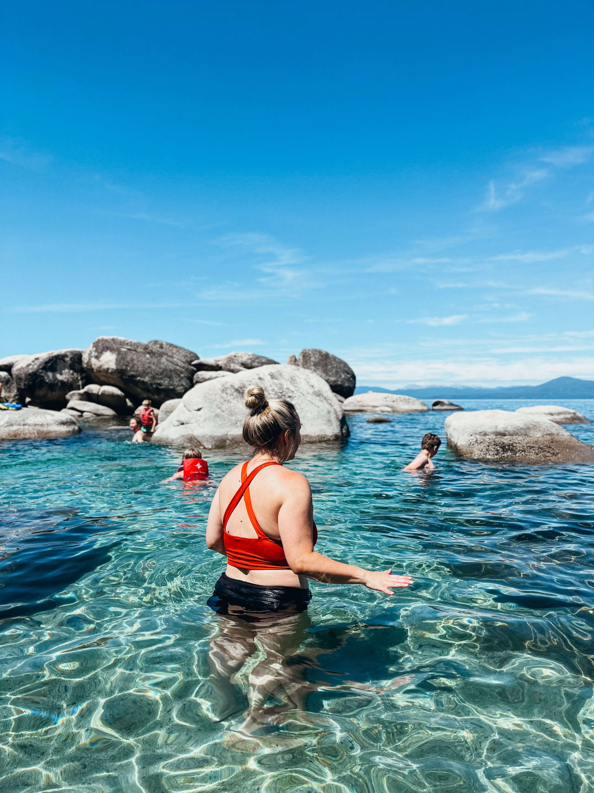 Woman stands in clear blue water with large boulders near Sand Harbor Beach
