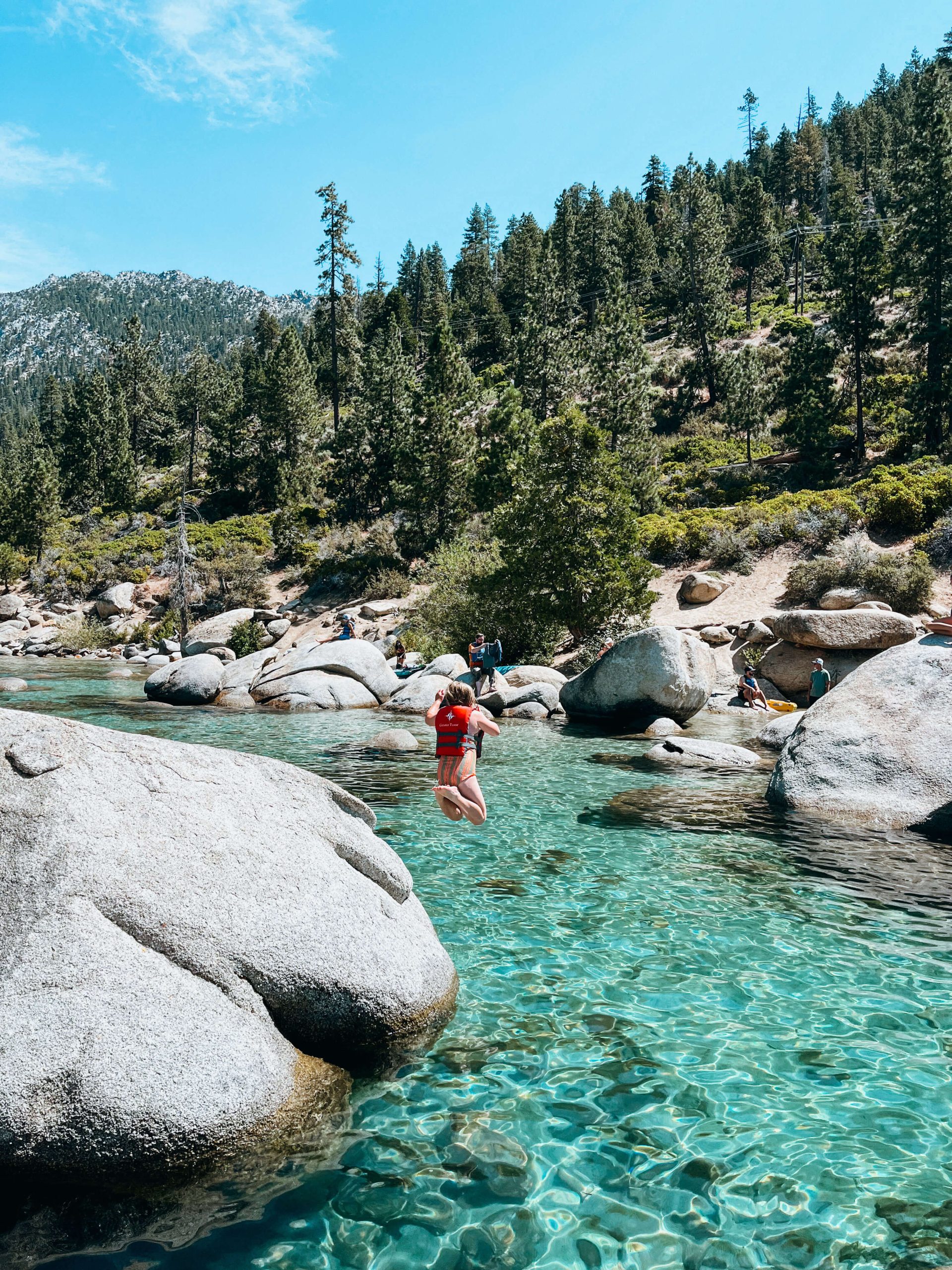 Child jumps from large boulder into clear green water near Bonsai Rock near Sand Harbor State Park