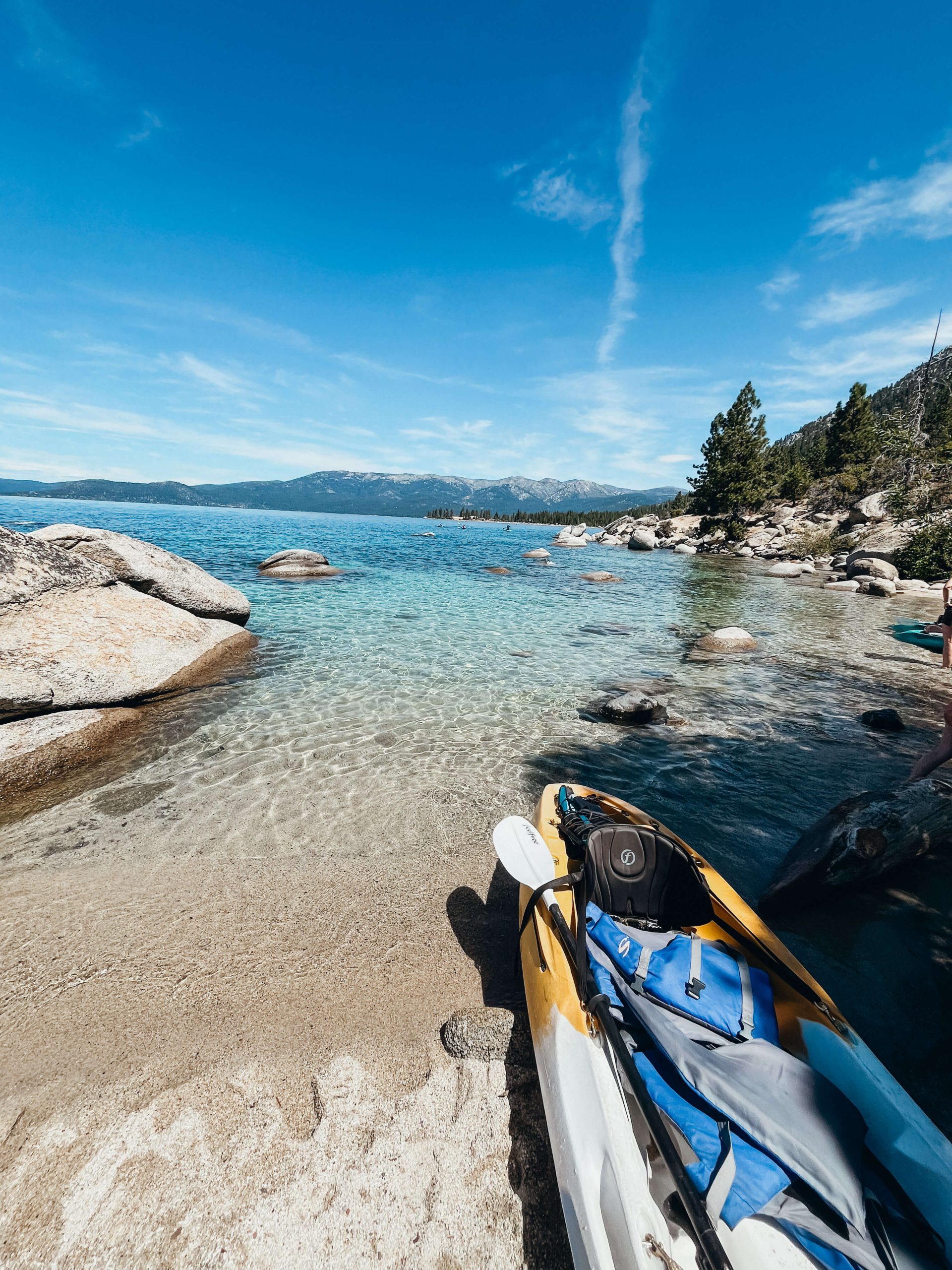Kayak pulled up on a sandy beach next to clear blue and green water 