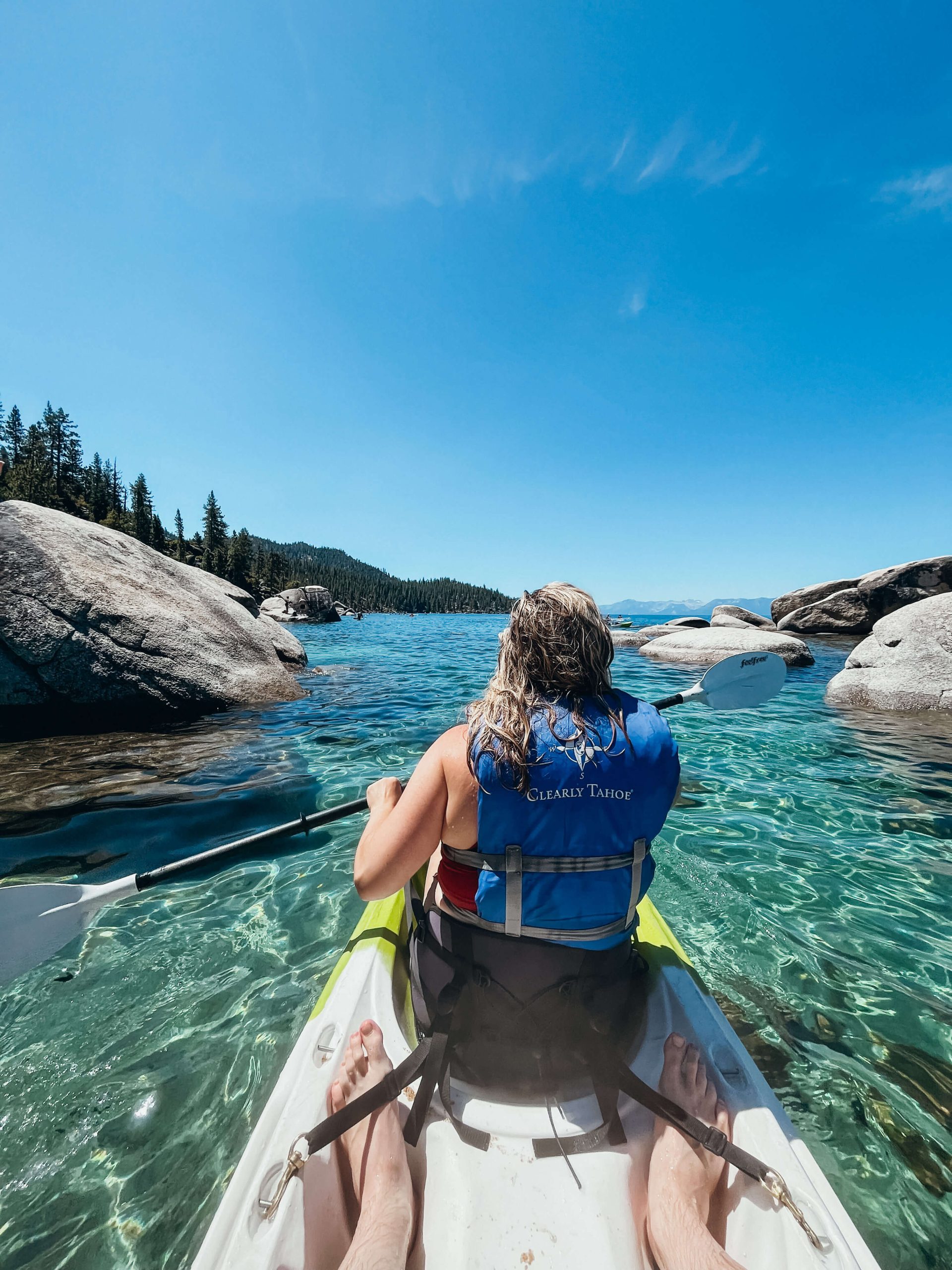 Woman in kayak paddling through clear green and blue water surrounded by boulders near Sand Harbor State Park