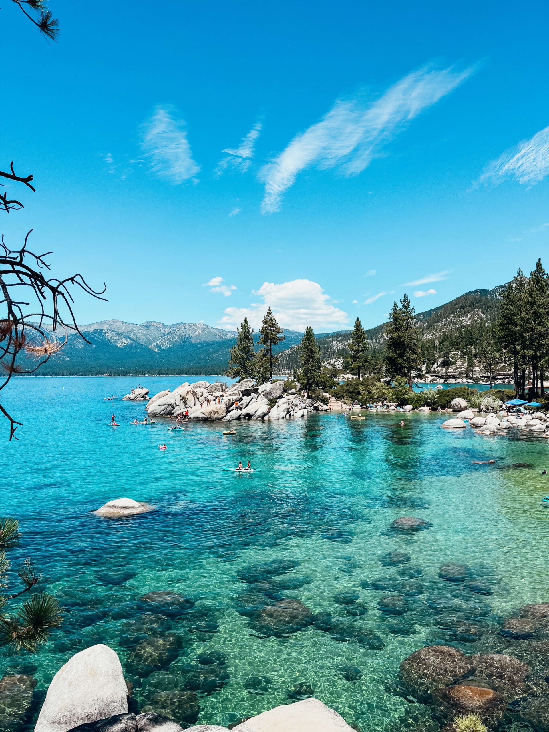 Clear blue and green water with kayakers and paddle boarders with coast lined with granite rocks and pine trees at Sand Harbor State Park Beach