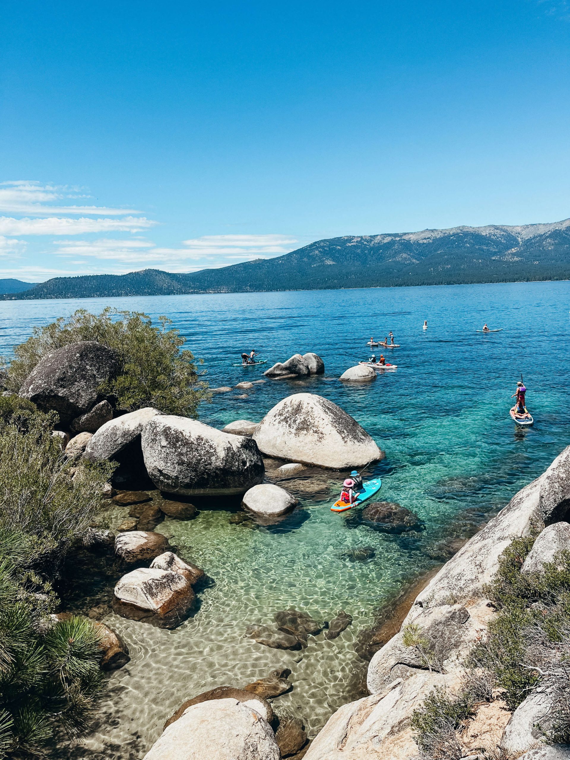Kayakers and paddleboarders in clear water with large boulders at Sand Harbor State Park