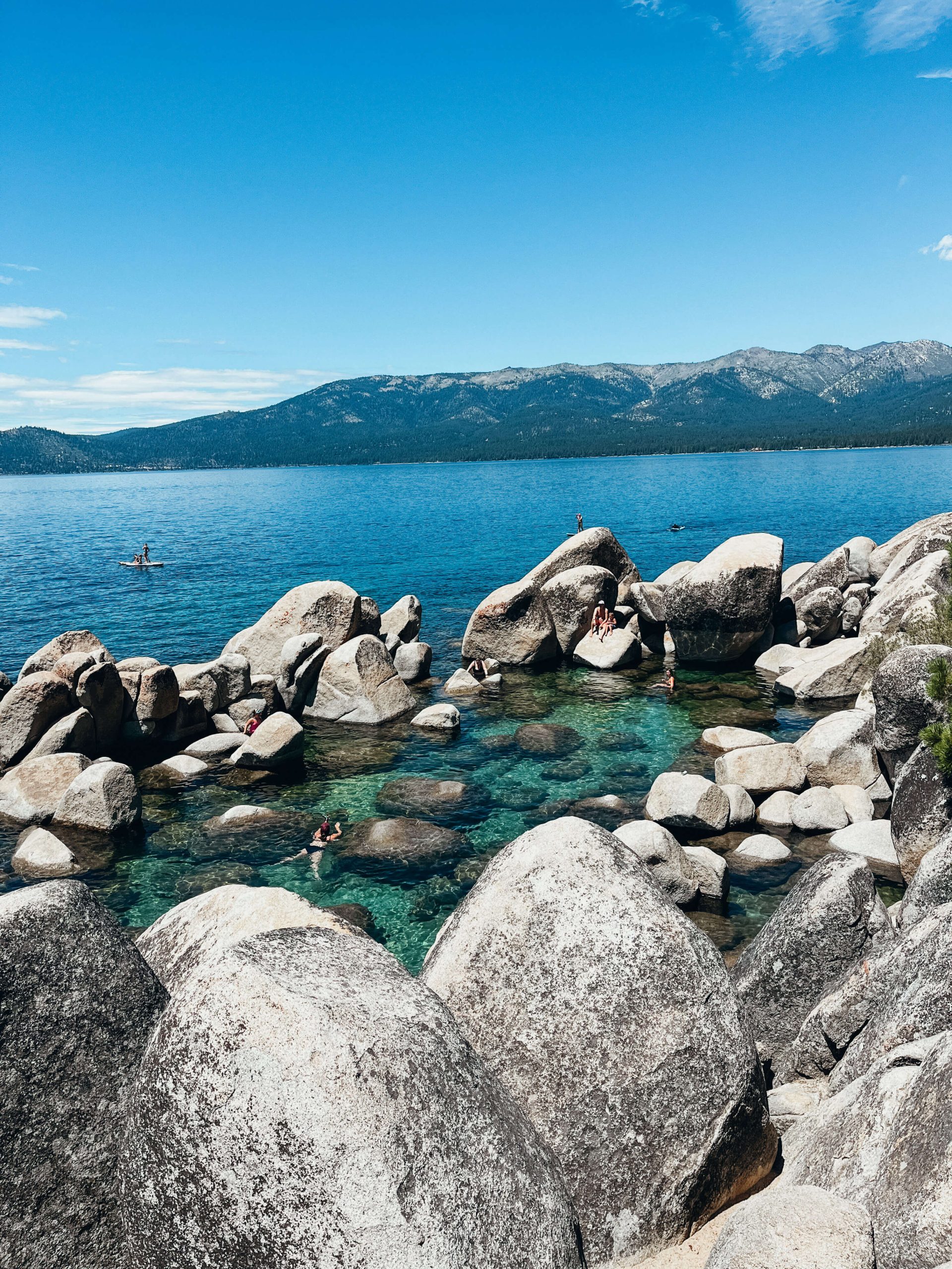 Large circle of boulders in clear green water with people swimming at Sand Harbor State Park