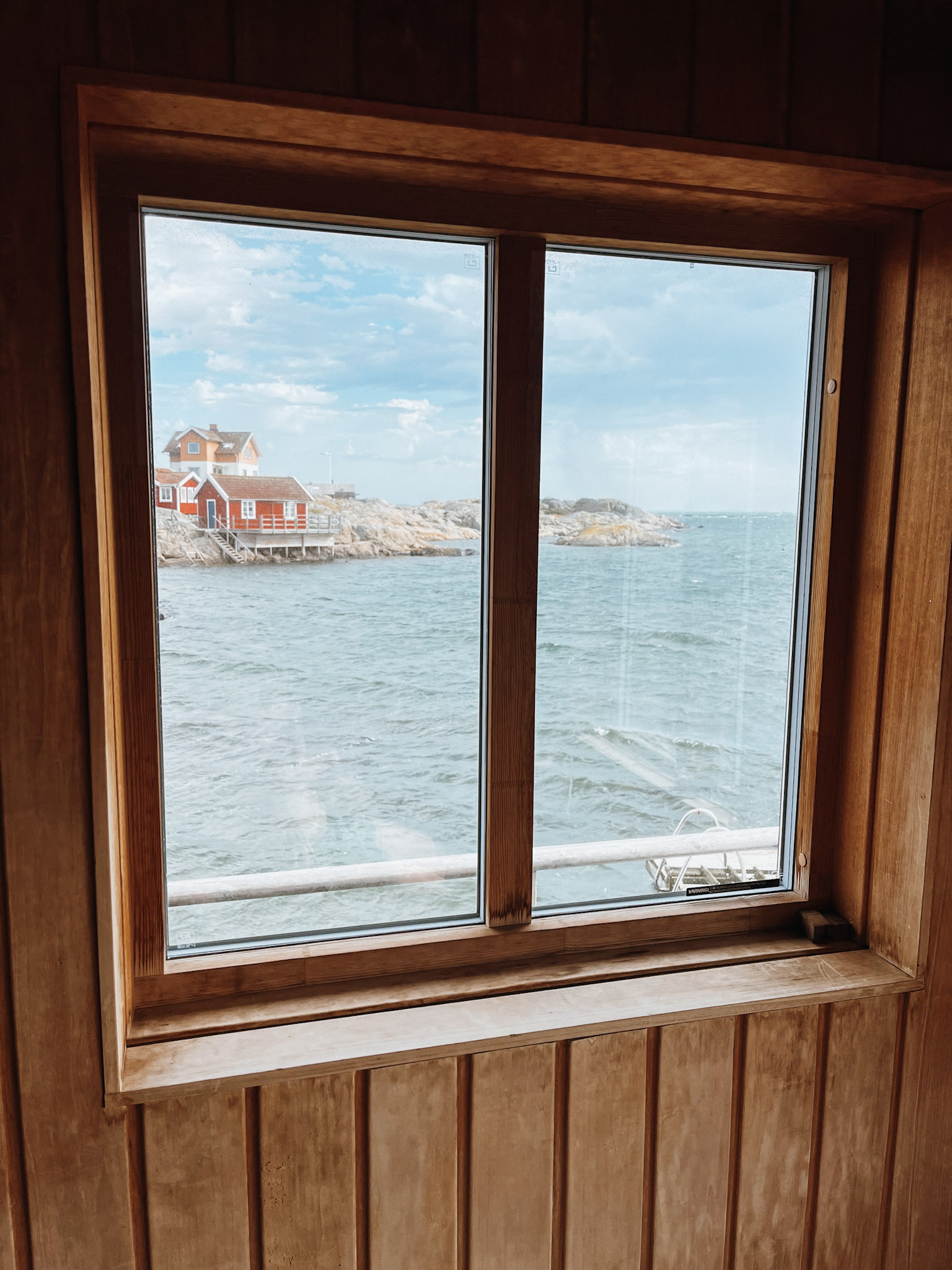 Looking out of window from inside the sauna on Fotö out to red and white buildings built on the rocks