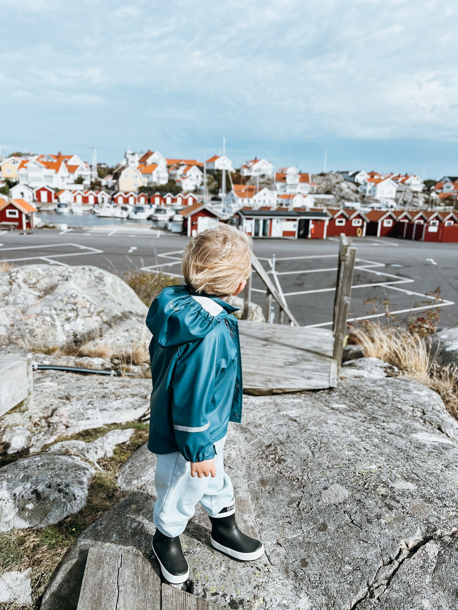Child stands on smooth rocks with red and white buildings behind him near Hönö Sweden