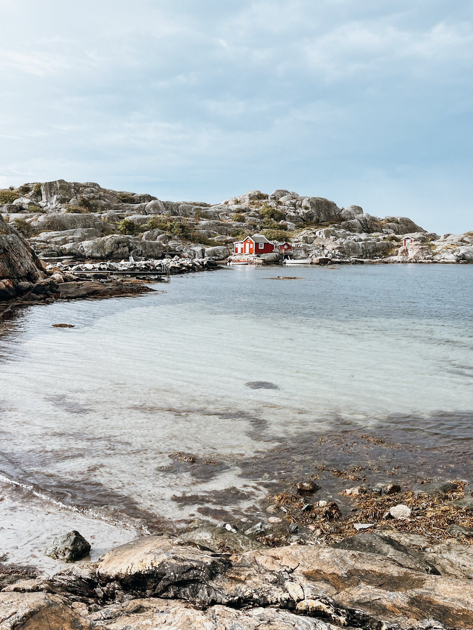 Clear water next to rocky coastline with a red fishing hut on Hönö Island (Bådevi)