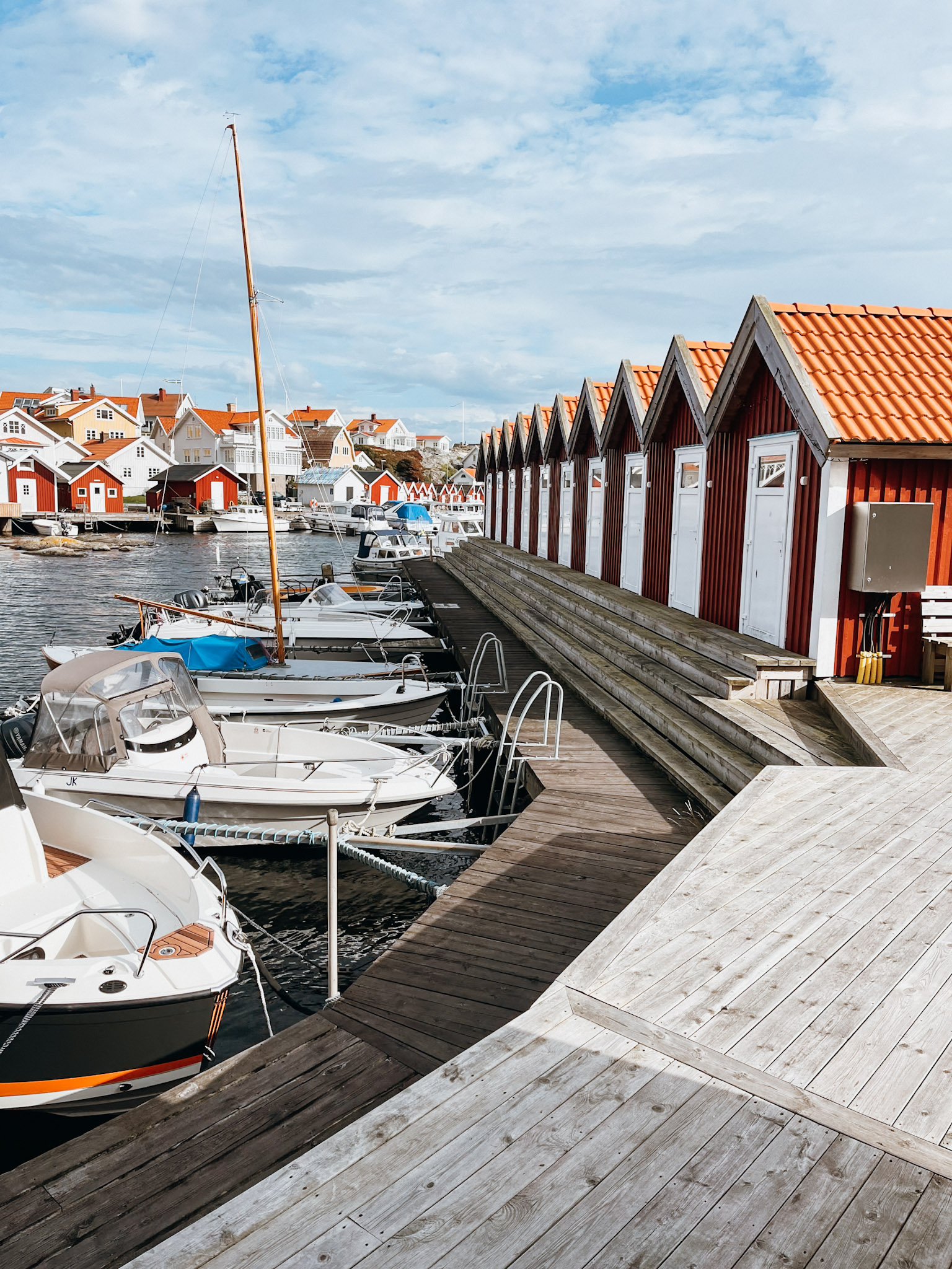 Row of red boat houses lining a dock with white boats tied up to the dock on Fotö Island near Gothenburg