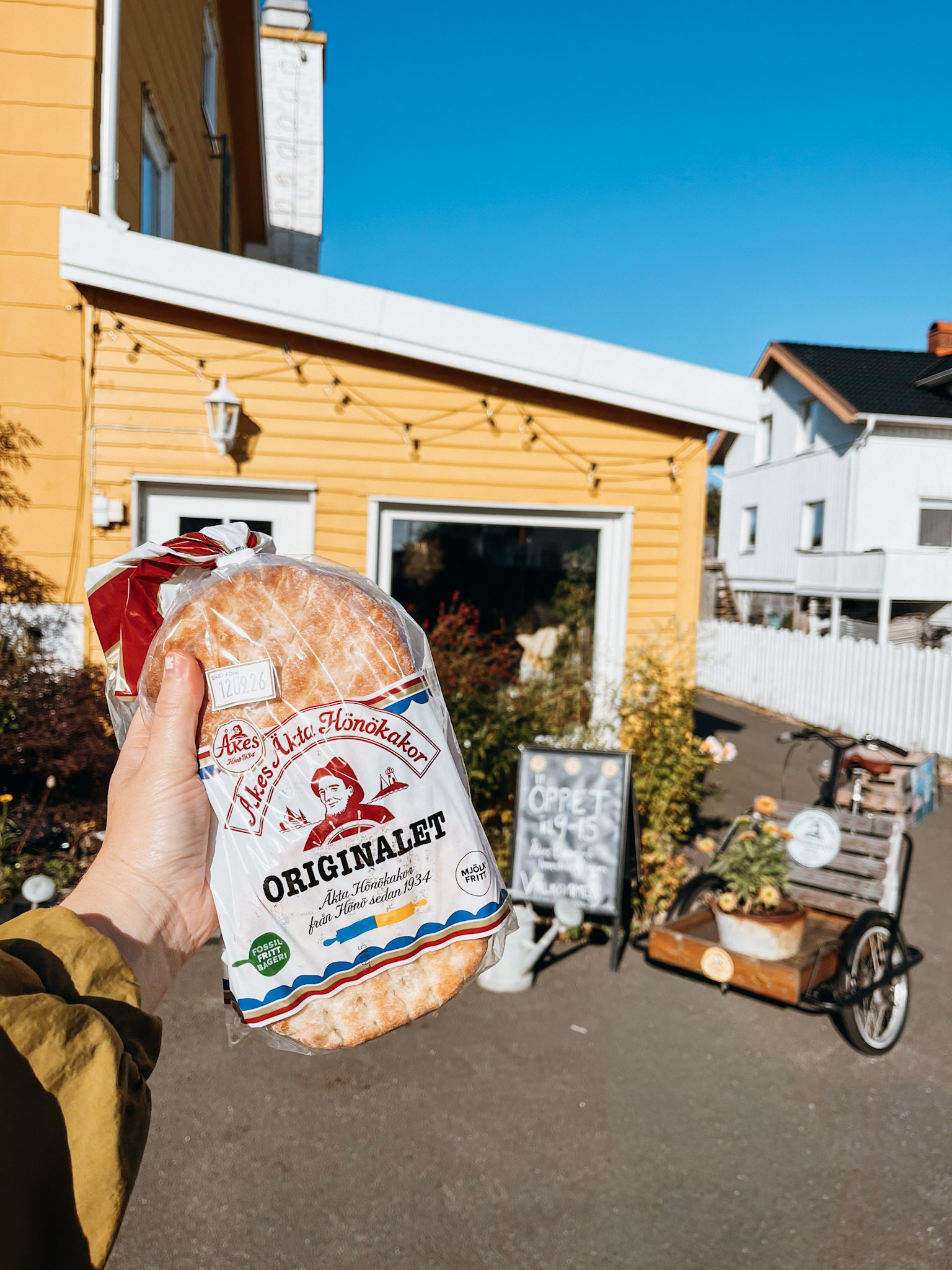 A hand holds up a bag of bread in front of a yellow house on Hönö Island Sweden