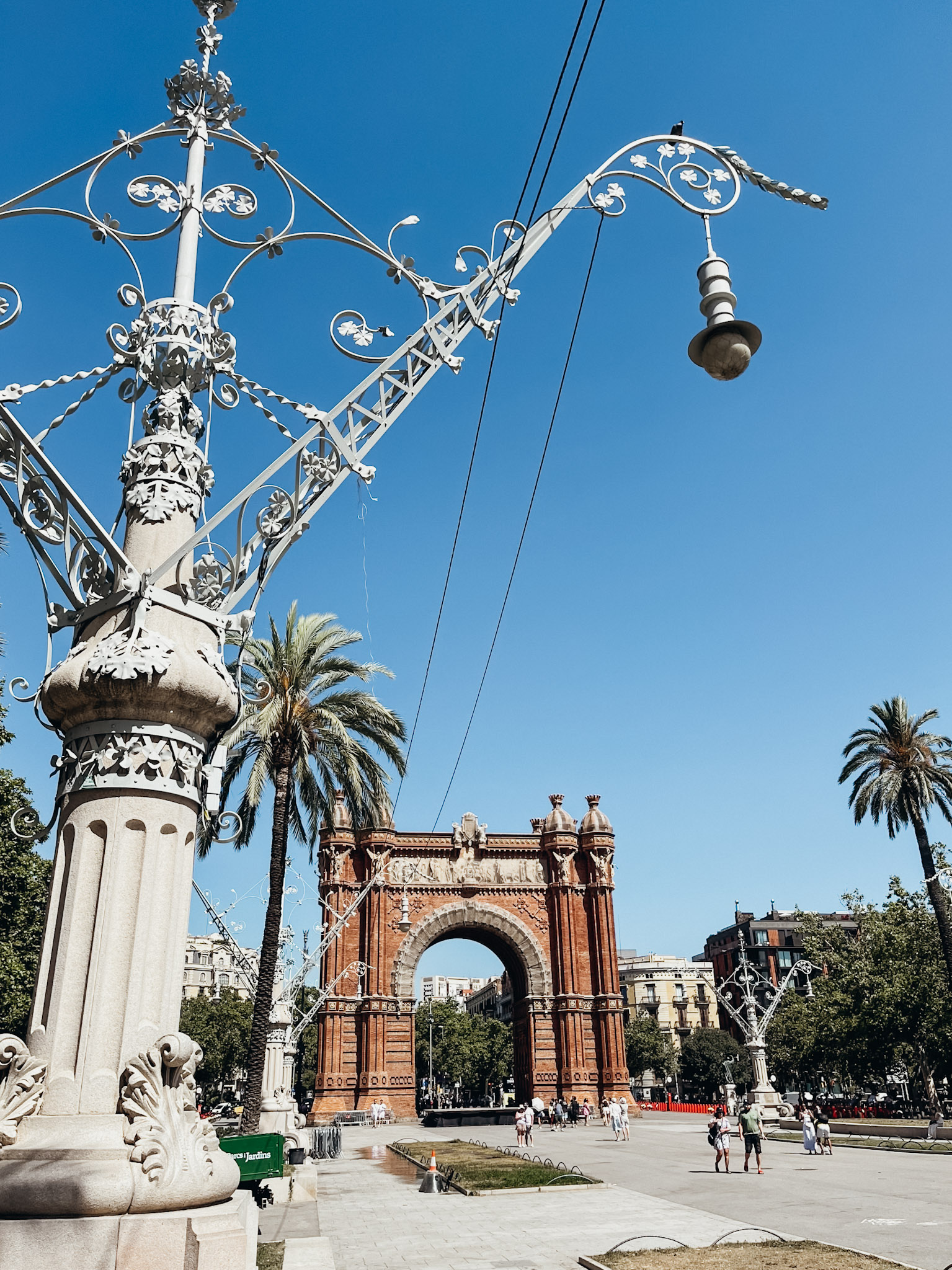 Large brown arch at end of promenade lined with palm trees in barcelona in June